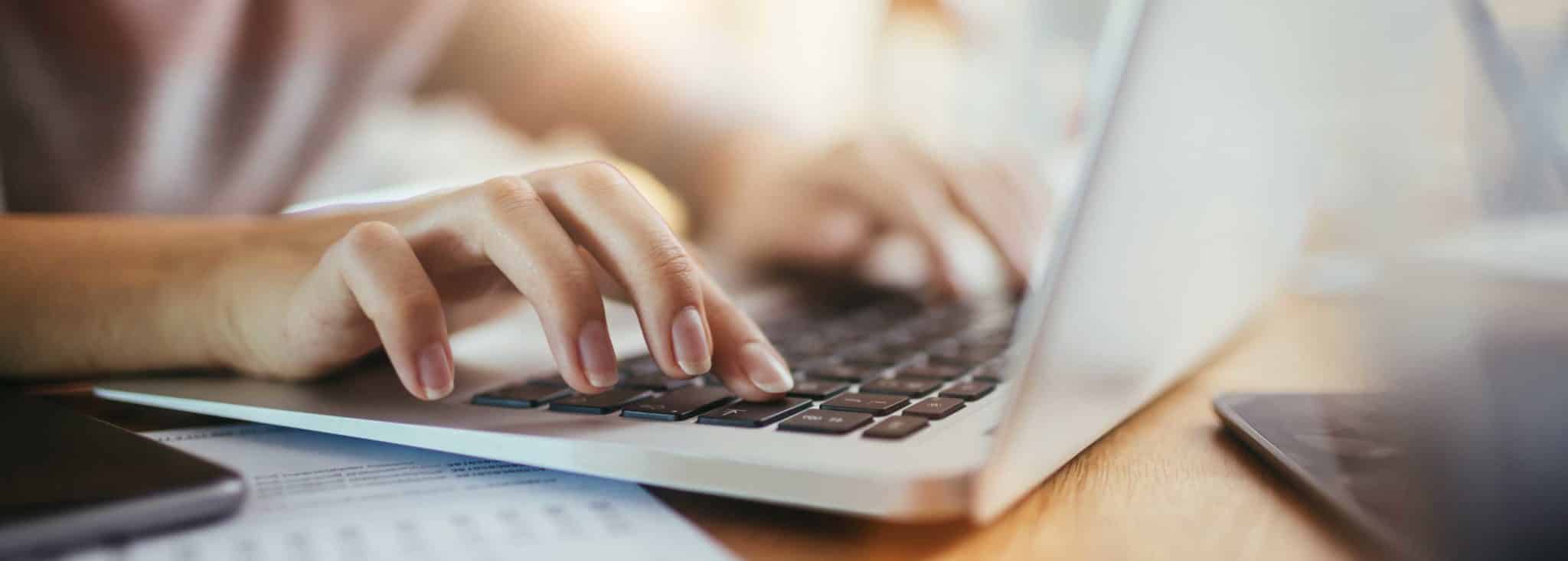 Eine Person tippt auf der Tastatur eines Laptops, während sie auf einem Tisch sitzt.
