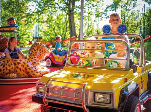 Gelbes Kinderauto mit zwei Kindern, die im Fahrzeug sitzen und spielen, auf einem Karussell.